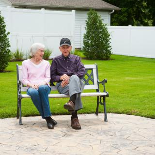 An elderly couple sitting on a bench in a garden setting.