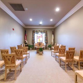 Small chapel interior with arranged seating, a stained glass window, and a central cross.