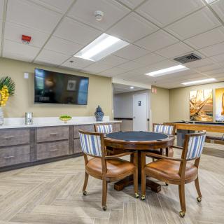 A modern room featuring a round table and chairs, with a wall-mounted television and sleek kitchenette.