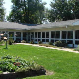 A one-story building surrounded by a well-maintained lawn and garden with trees in the background.