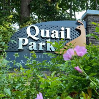 Entrance sign for Quail Park surrounded by lush greenery and flowers.