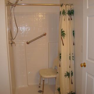 An accessible bathroom shower equipped with a grab bar and shower chair.