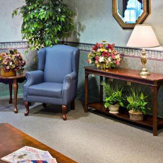 A cozy living room corner with a blue armchair, decorative plants, and a lamp on a console table.