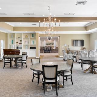 A spacious and modern dining area featuring multiple tables and chairs, elegant chandeliers, and a cozy carpeted floor.