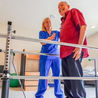 A nurse assists an elderly man with physical therapy using a walking aid.