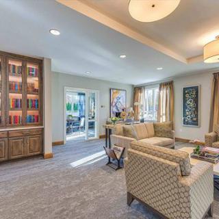 A modern living room featuring comfortable seating, a well-organized bookshelf, and ample natural light.
