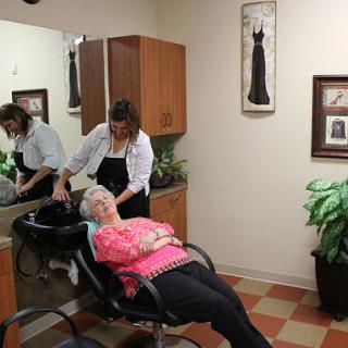 A hairstylist provides a hair treatment to an elderly woman in a cozy salon environment.