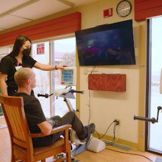 A rehabilitation session where a patient engages in exercise while watching a television screen, guided by a healthcare professional.
