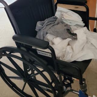 An unused wheelchair with some clothing draped over it.