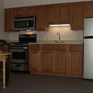 A modern kitchen with wooden cabinets, featuring a microwave, oven, sink, and refrigerator.