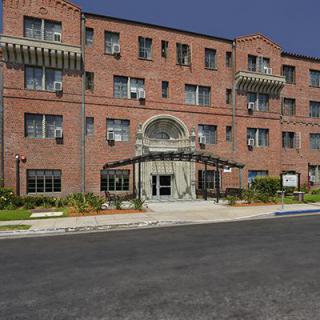 A brick apartment building with a central entrance and landscaped surroundings.