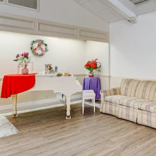 A cozy living room featuring a white piano, a striped sofa, and decorative floral arrangements on tables.