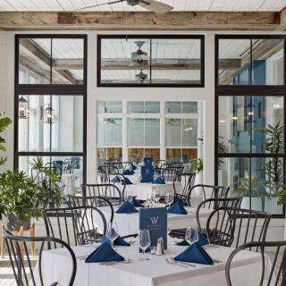 A stylish restaurant dining area with neatly arranged tables and chairs, featuring elegant blue napkins and large windows.