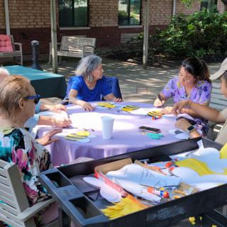 A group of seniors engaged in an outdoor crafting activity around a table.
