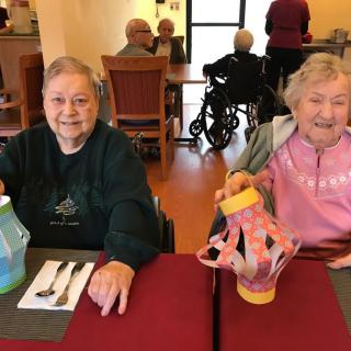 Two elderly women smiling and enjoying a meal together in a dining area.
