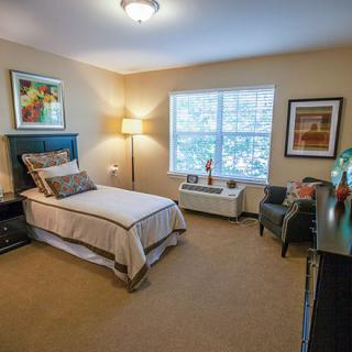 A cozy bedroom with a single bed, lamp, window, and decorative elements.