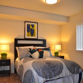A modern bedroom with stylish decor, featuring a neatly made bed, two lamps on nightstands, and artwork above the headboard.
