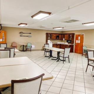 A spacious dining area with several tables and chairs, featuring a small kitchen in the background.