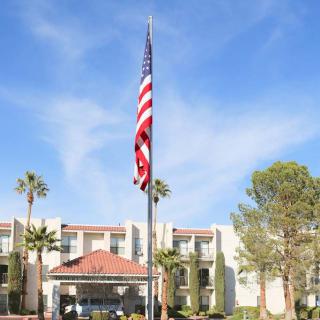 An American flag flying in front of a building surrounded by palm trees under a clear blue sky.