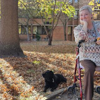 An elderly woman enjoying a sunny autumn day with her dog by her side.