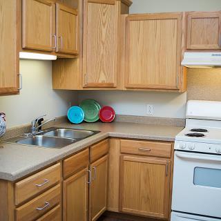 A compact kitchen with wooden cabinets, a stove, and a double sink.