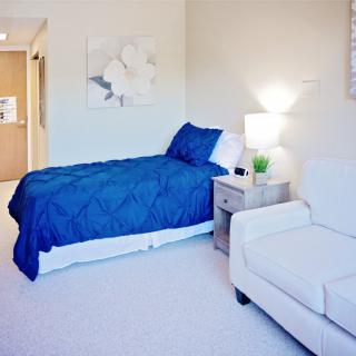A minimalist bedroom with a blue bedspread, white furniture, and soft lighting.