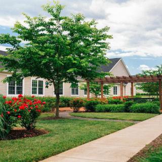 A scenic view of a house with a beautifully landscaped garden featuring trees, shrubs, and a flower bed along a sidewalk.