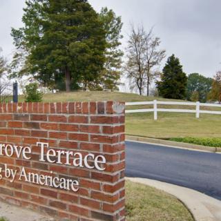 A brick sign at the entrance of Grove Terrace, surrounded by grassy areas and trees under an overcast sky.