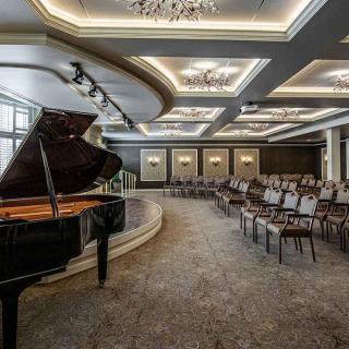 An elegant concert hall interior featuring a grand piano on stage and arranged seating.
