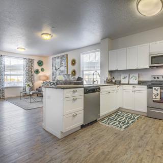 A modern kitchen with an open floor plan connecting to a cozy living area, featuring white cabinets and hardwood flooring.