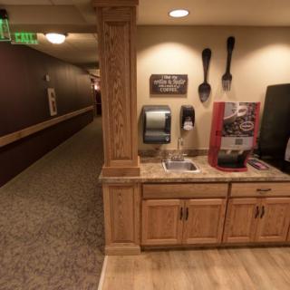 A hallway with a coffee station featuring wooden cabinets and decorative utensils on the wall.