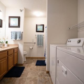 A spacious bathroom with a laundry area, featuring a washing machine, double sink vanity, and neatly arranged towels.
