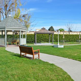A peaceful park scene with a gazebo, bench, and paved pathway on a sunny day.