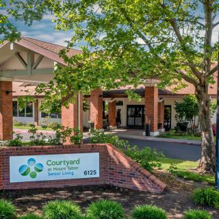 Entrance of a building with signage and surrounding trees and landscaping.
