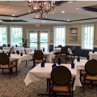 An elegant dining room with neatly arranged tables and chairs, featuring white tablecloths and a chandelier.