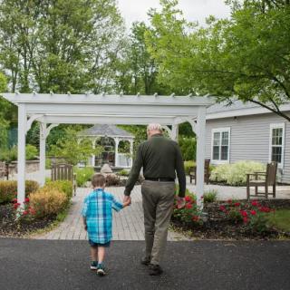 A grandfather and grandchild holding hands while walking through a garden.