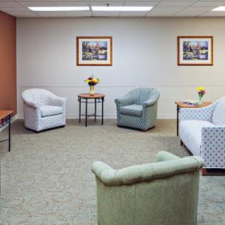 A cozy waiting room with several comfortable chairs and small tables, adorned with decorative paintings on the walls.