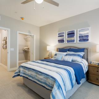 A modern bedroom with a blue and white color scheme featuring a neatly made bed, bedside tables, and wall art.