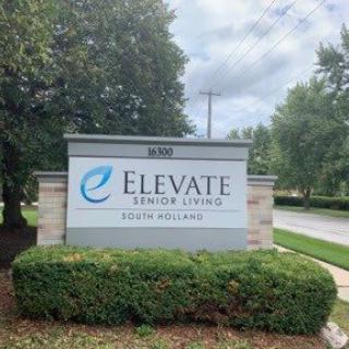 A sign for Elevate Senior Living surrounded by greenery.