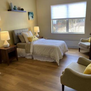 A cozy bedroom with a bed, nightstands, and chairs in a softly lit room.