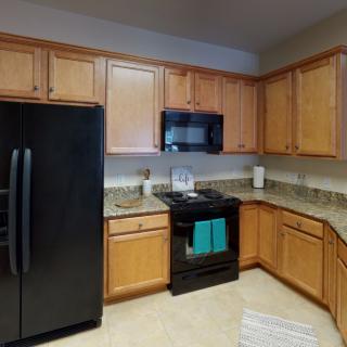 A modern kitchen with wooden cabinets, black appliances, and tiled flooring.