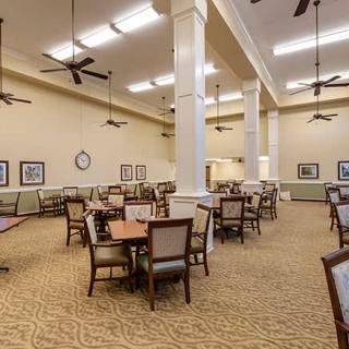 An elegant dining room with tables and chairs, featuring ceiling fans and warm lighting.