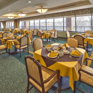 A well-decorated dining room with neatly arranged tables and chairs, featuring yellow tablecloths and a scenic view through large windows.