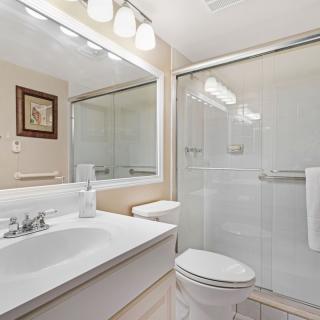 A clean and modern bathroom with a large mirror, sink, toilet, and shower.