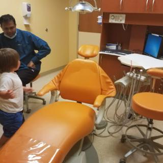 A child explores a dental clinic with an adult in the background.