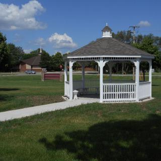 A white gazebo situated in a sunny park with lush green grass and clear blue skies.