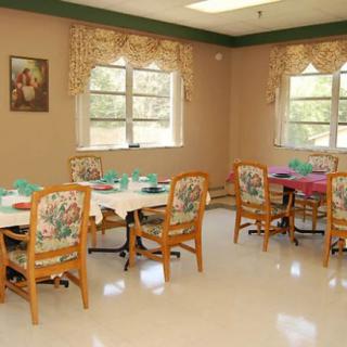 A cozy dining room with decorated chairs and set tables, illuminated by natural light through the windows.