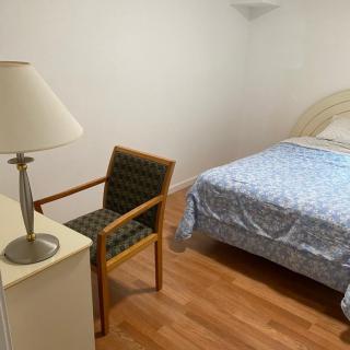 A minimalist bedroom featuring a bed, chair, lamp, and wooden flooring.