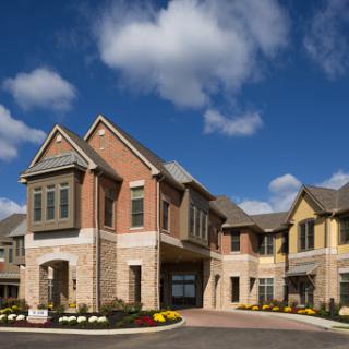 A modern multi-unit residential building with attractive architecture and colorful landscaping under a blue cloudy sky.