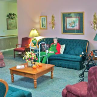 An elderly person sitting on a sofa in a cozy living room with a walker nearby.